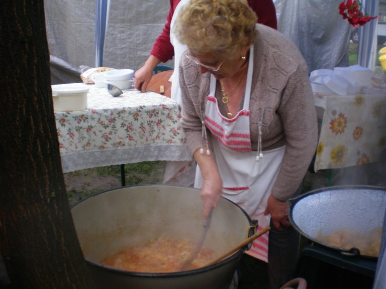 Starsza kobieta miesza potrawę z kapusty w bardzo dużym garnku.