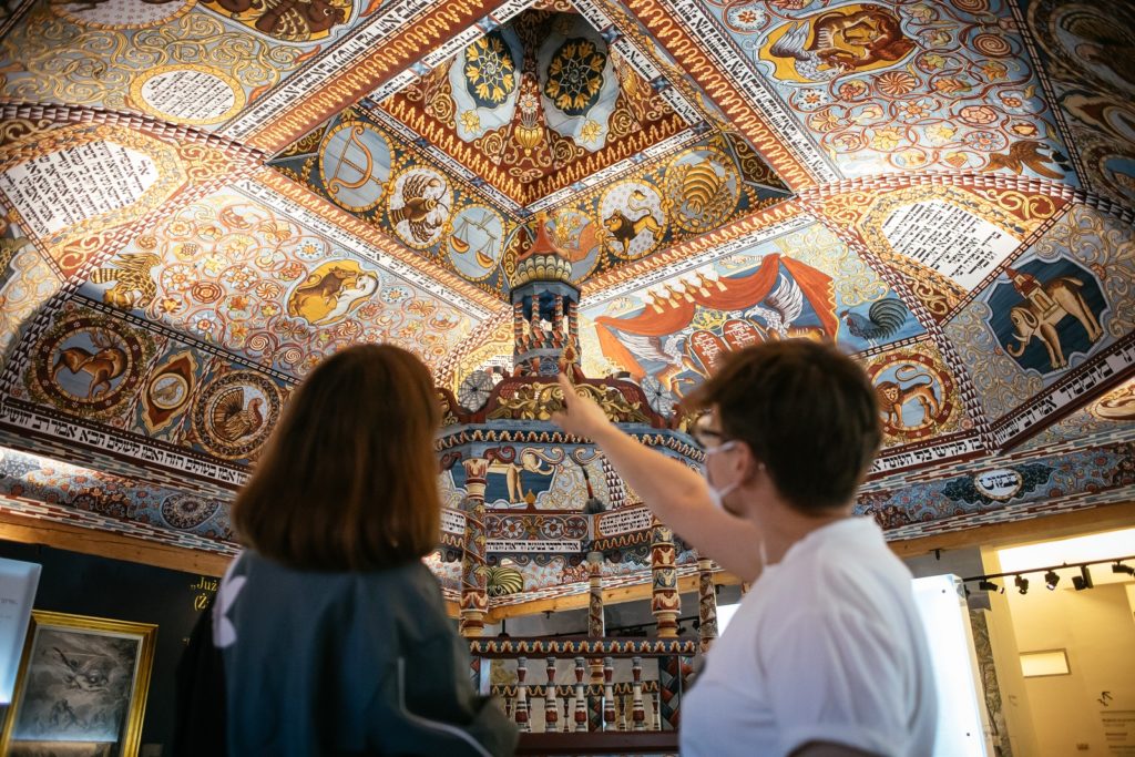 Dwie osoby podziwiają malowane sklepienie zrekonstruowanej synagogi z Gwoźdźca, która znajduje się w Muzeum POLIN.