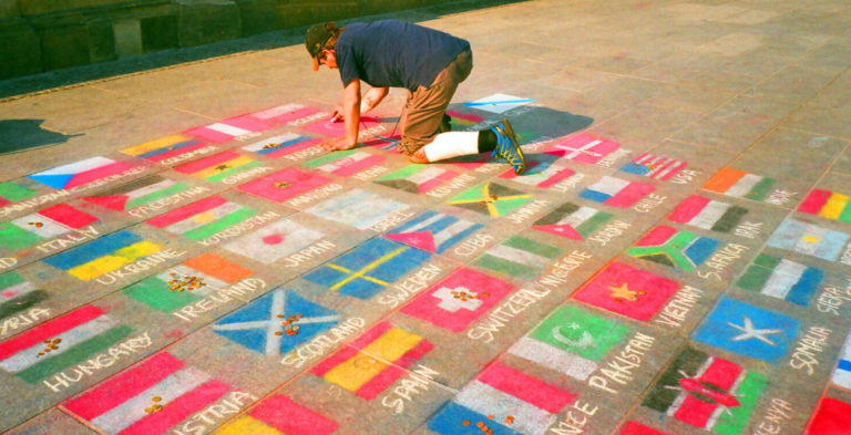 Mężczyzna rysuje kredą flagi równych państw na chodniku.