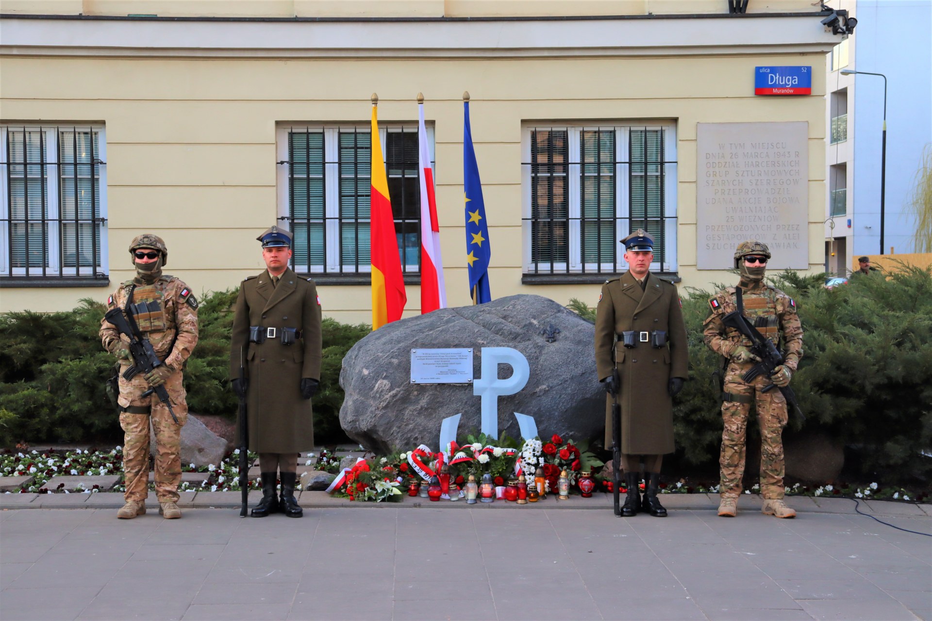 Grafika przedstawia żołnierzy przed pomnikiem.