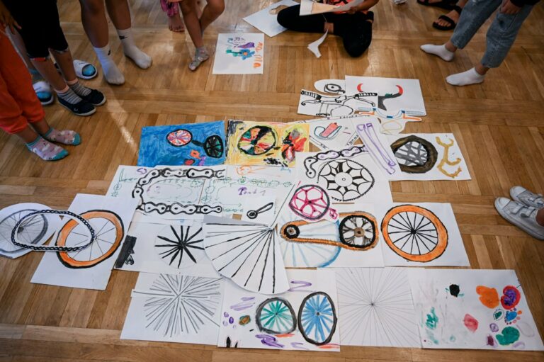 Prace rysunkowe prezentujące różne części roweru ułożone na podłodze.