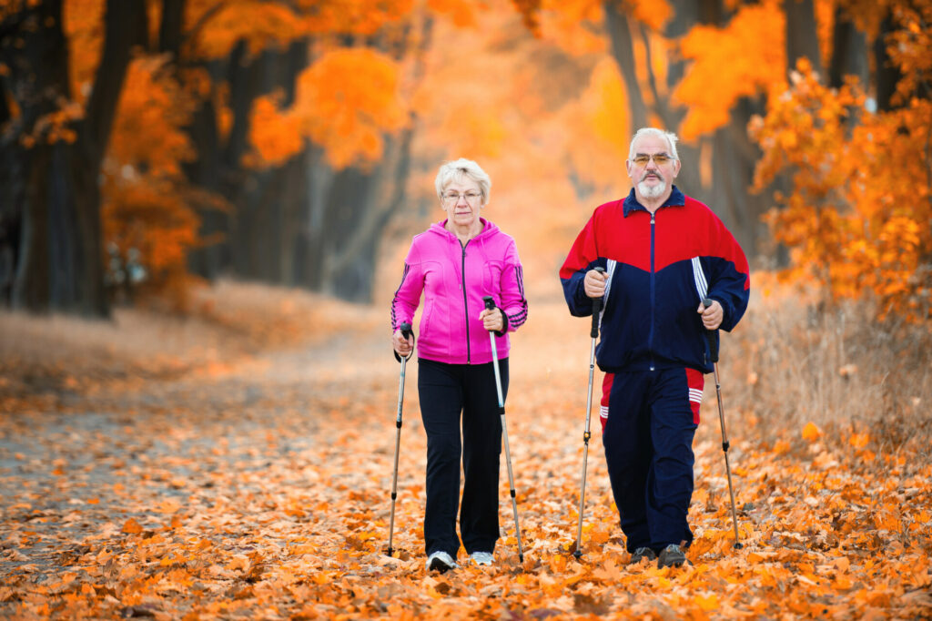 para seniorów maszeruje z kijkami do nordic walking, w tle drzewa w kolorach jesieni