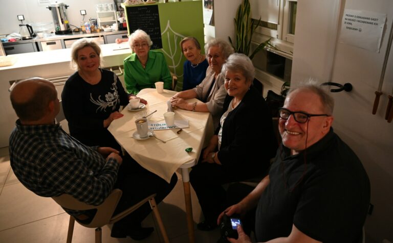 Zdjęcie przedstawia siedem osób siedzących przy stoliku.