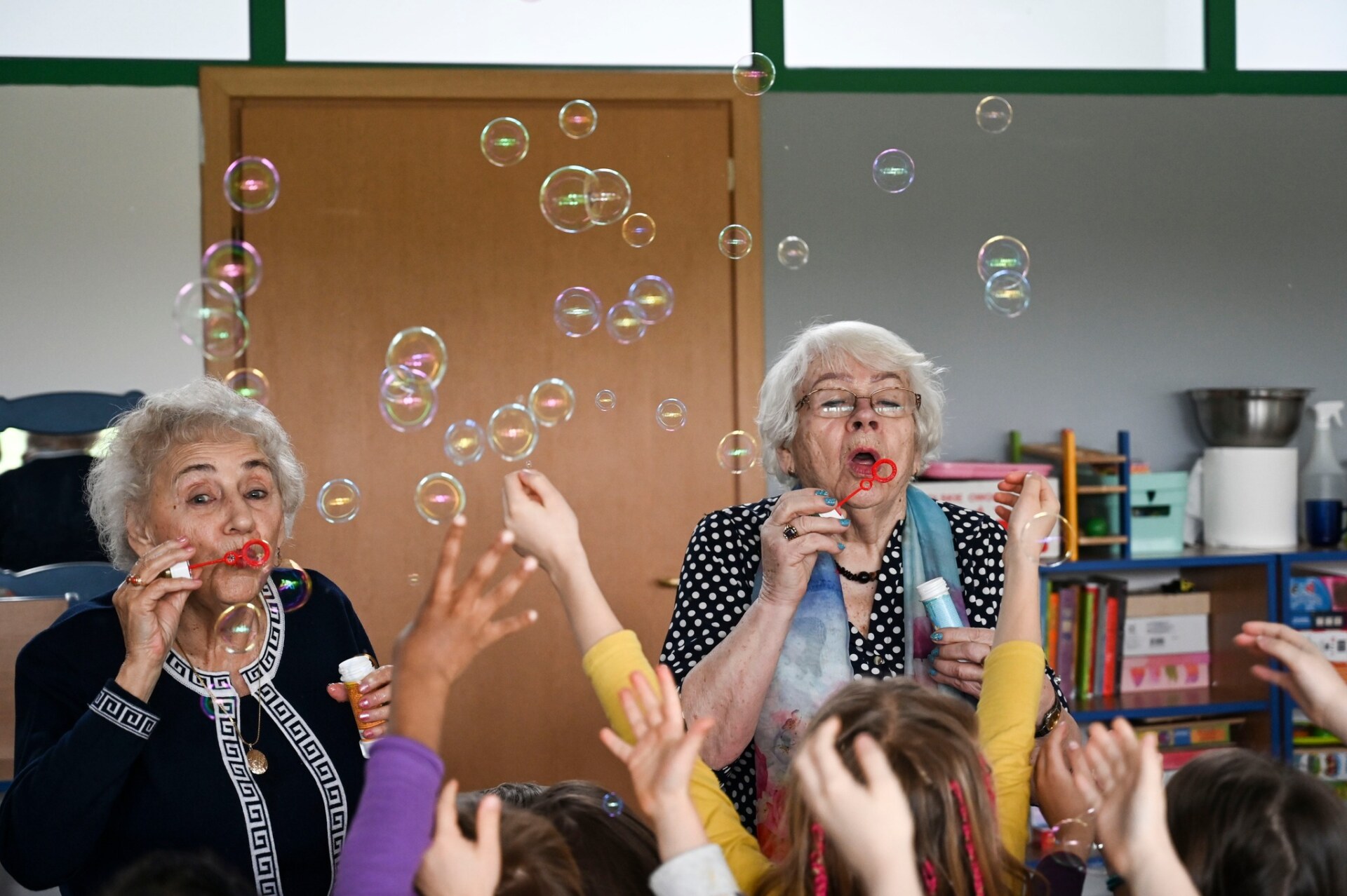 Dwie starsze kobiety puszczają bańki mydlane w przedszkolu.