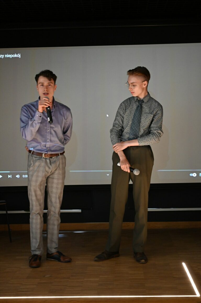 Zdjęcie przedstawia dwie osoby stojące na scenie.