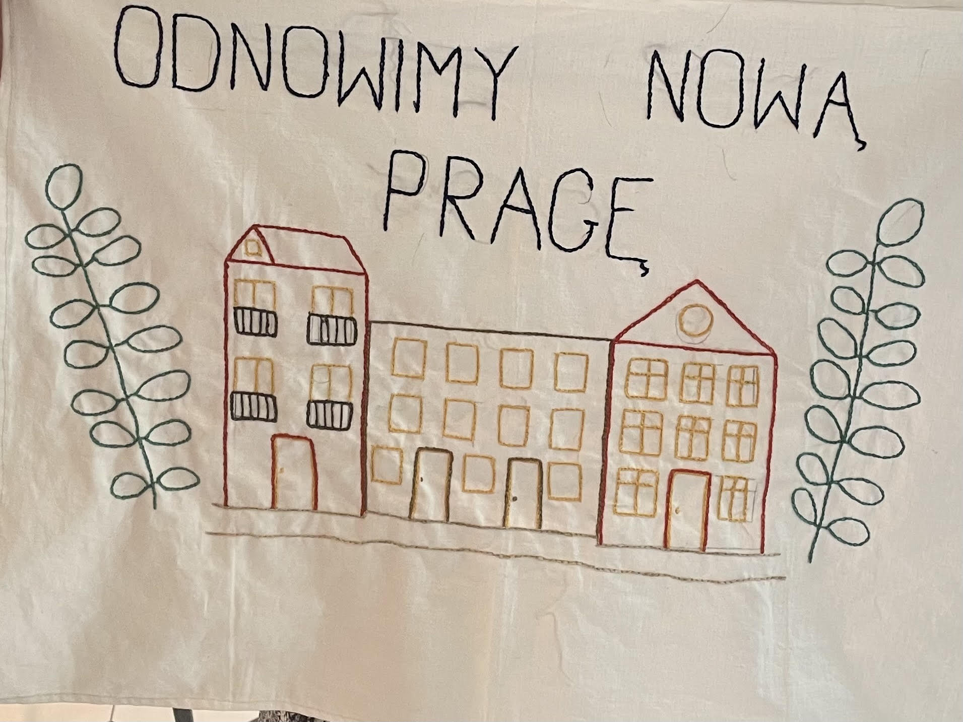 Zdjęcie przedstawia wyhaftowany rysunek budynku i napis odnowimy nową Pragę.