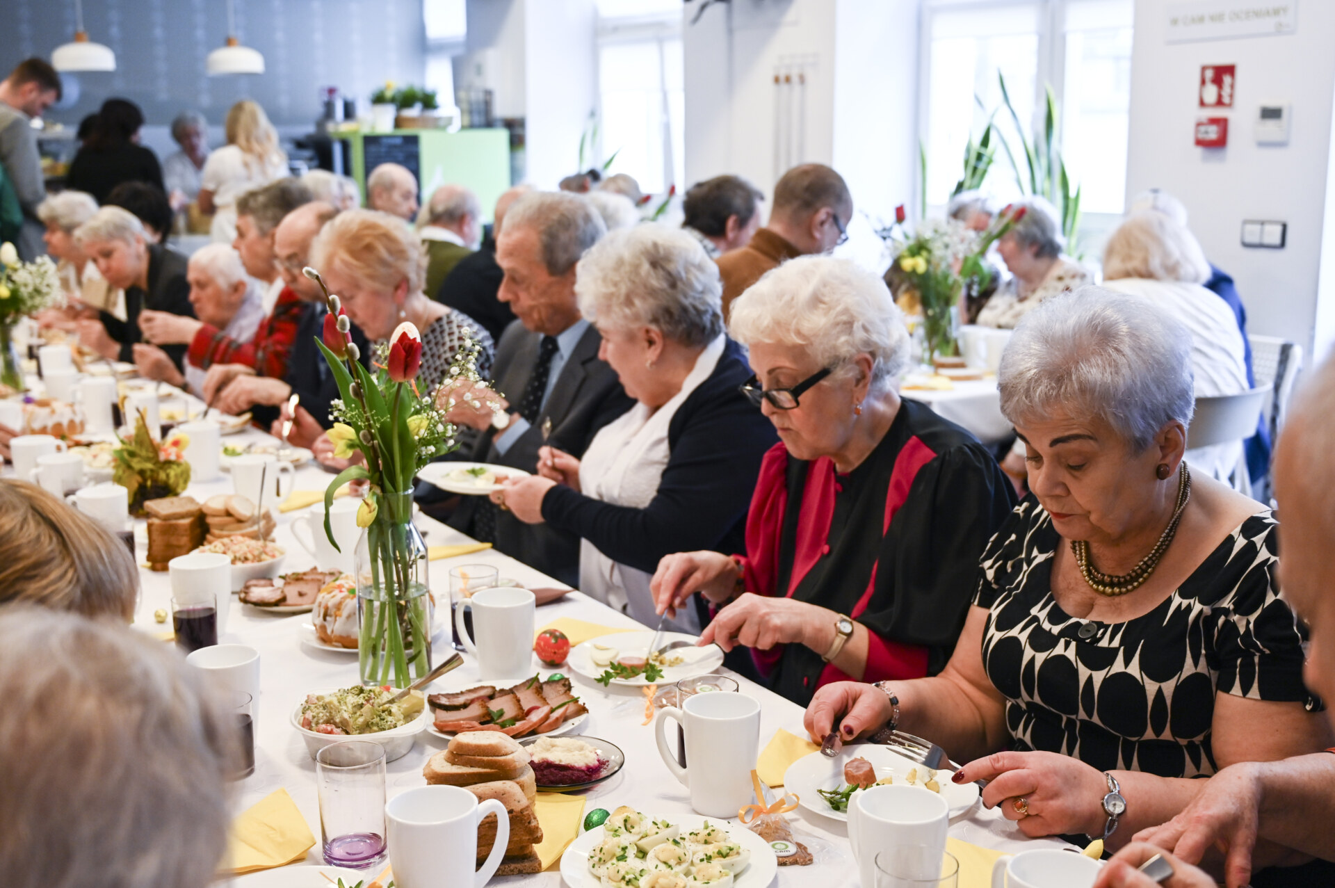 Grupa seniorów je obiad przy wspólnym, świątecznym stole.