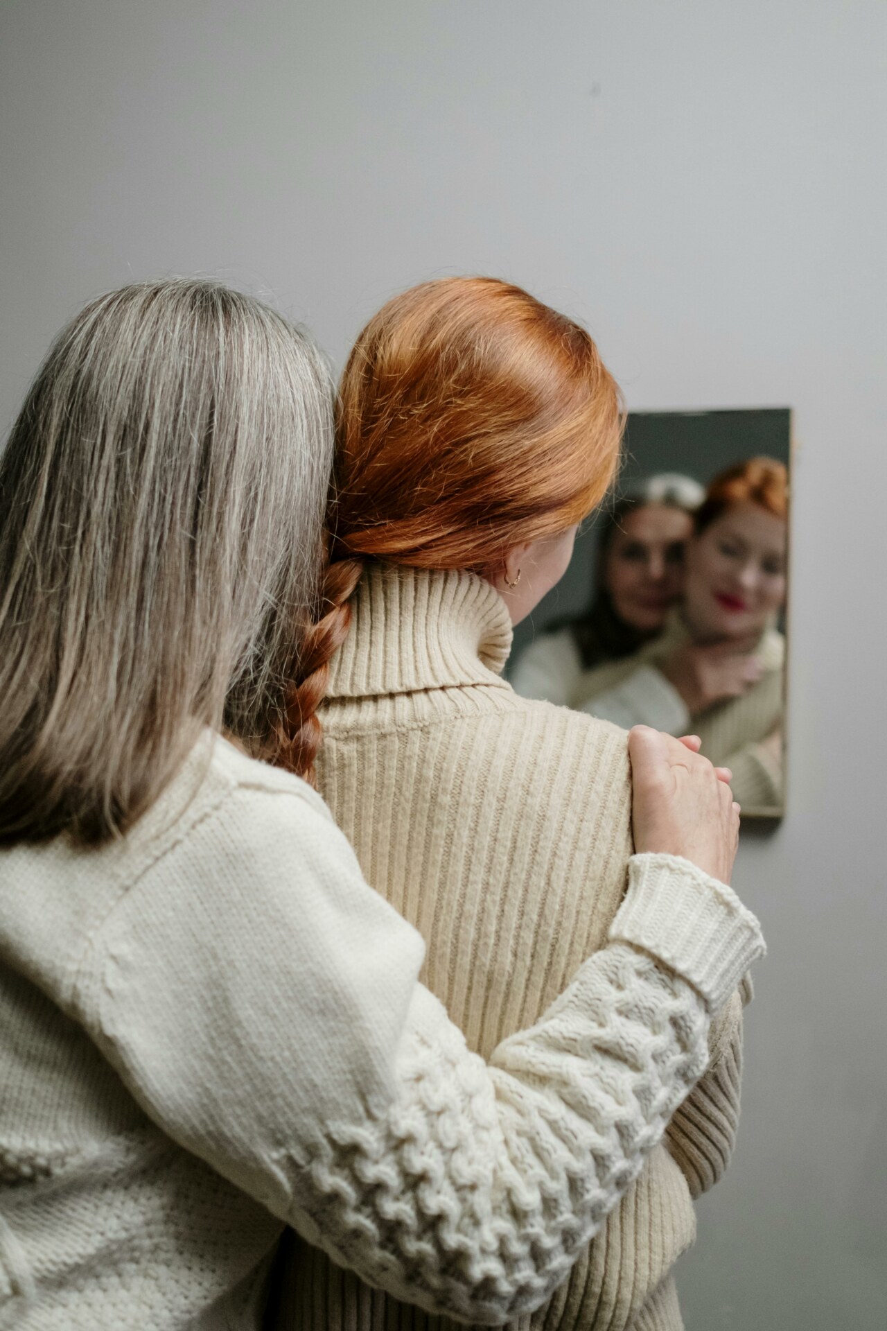 Dwie kobiety, młoda i starsza odwrócone tyłem patrzące w lustro.